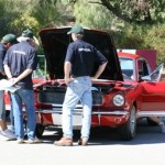 A group of men standing around a red mustang.