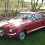 A red and white mustang is parked in the grass.