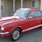 A red and white mustang is parked in front of a house.