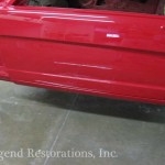 A red car is being painted in a garage.