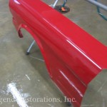 A red fender is being painted in a garage.