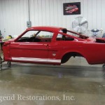 A red mustang is being restored in a garage.