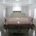 A pink car is being painted in a garage.