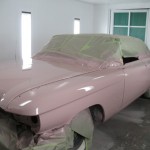 A pink car is being painted in a garage.