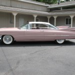 A pink classic car parked in front of a house.