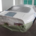 A white car is being painted in a garage.