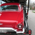 A red classic car is being transported on a flatbed truck.