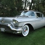 A silver classic car is parked in the grass.