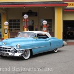 An old blue cadillac parked in front of a gas station.