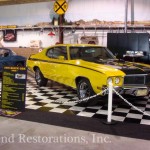 A yellow and blue muscle car is on display in a museum.