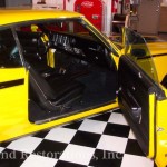 The door of a yellow muscle car is open.