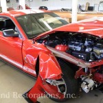 A red mustang with its hood open in a garage.