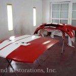 A red and white car is being painted in a garage.