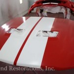 A red and white car is being painted in a garage.