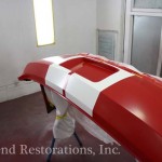 A red and white car being painted in a garage.