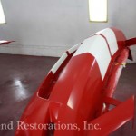 A red and white airplane being painted in a garage.