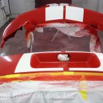 A red and white car being painted in a garage.