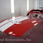 A red and white hood is being painted in a garage.