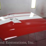 A red and white hood is being painted in a garage.