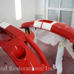 A red and white car is being painted in a garage.