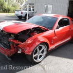 A red mustang with its hood open is parked in a garage.