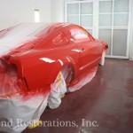 A red mustang is being painted in a garage.